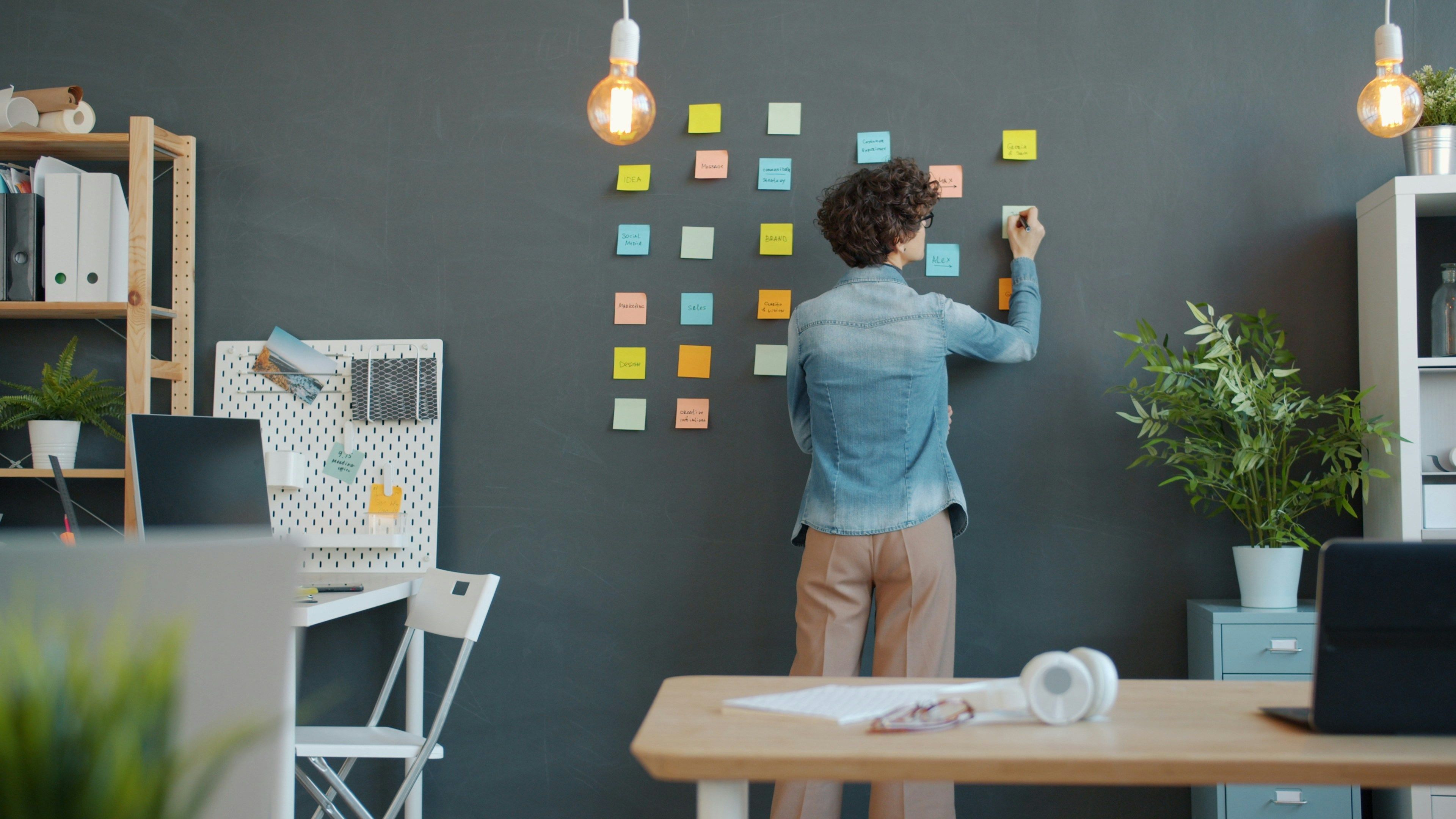 A man is attaching colorful sticky notes to a wall while writing on them.
